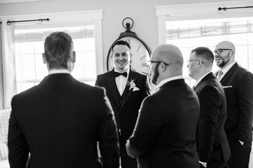 Black and white photo of groom smiling with groomsmen in tuxedos before wedding ceremony.