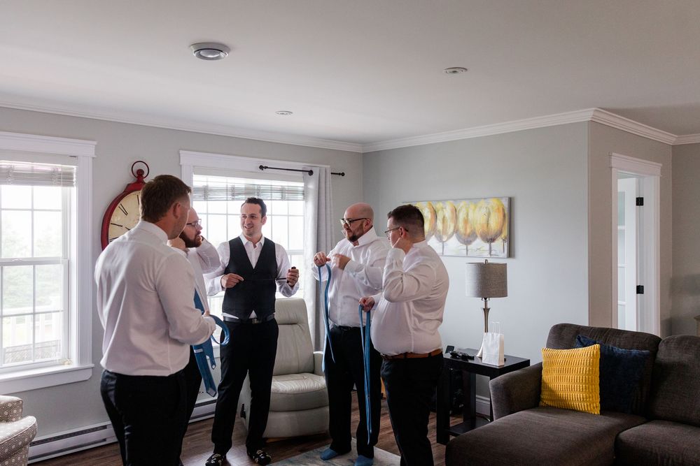 Groomsmen in white dress shirts getting ready together in an elegant living room before a wedding ceremony.