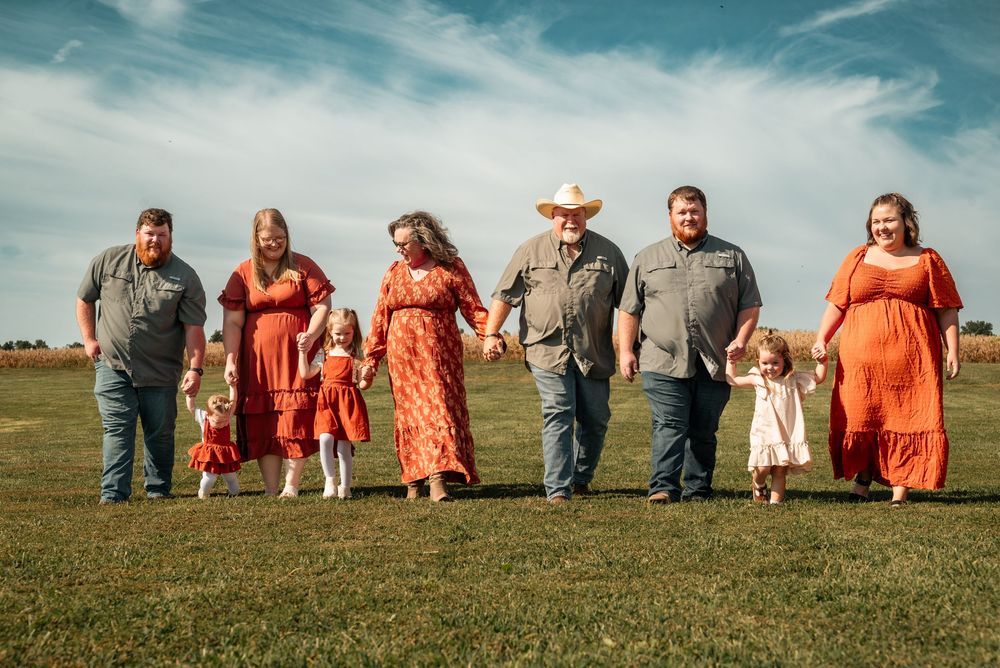 Large family in coordinating red outfits poses together on green field under blue sky for professional photo.