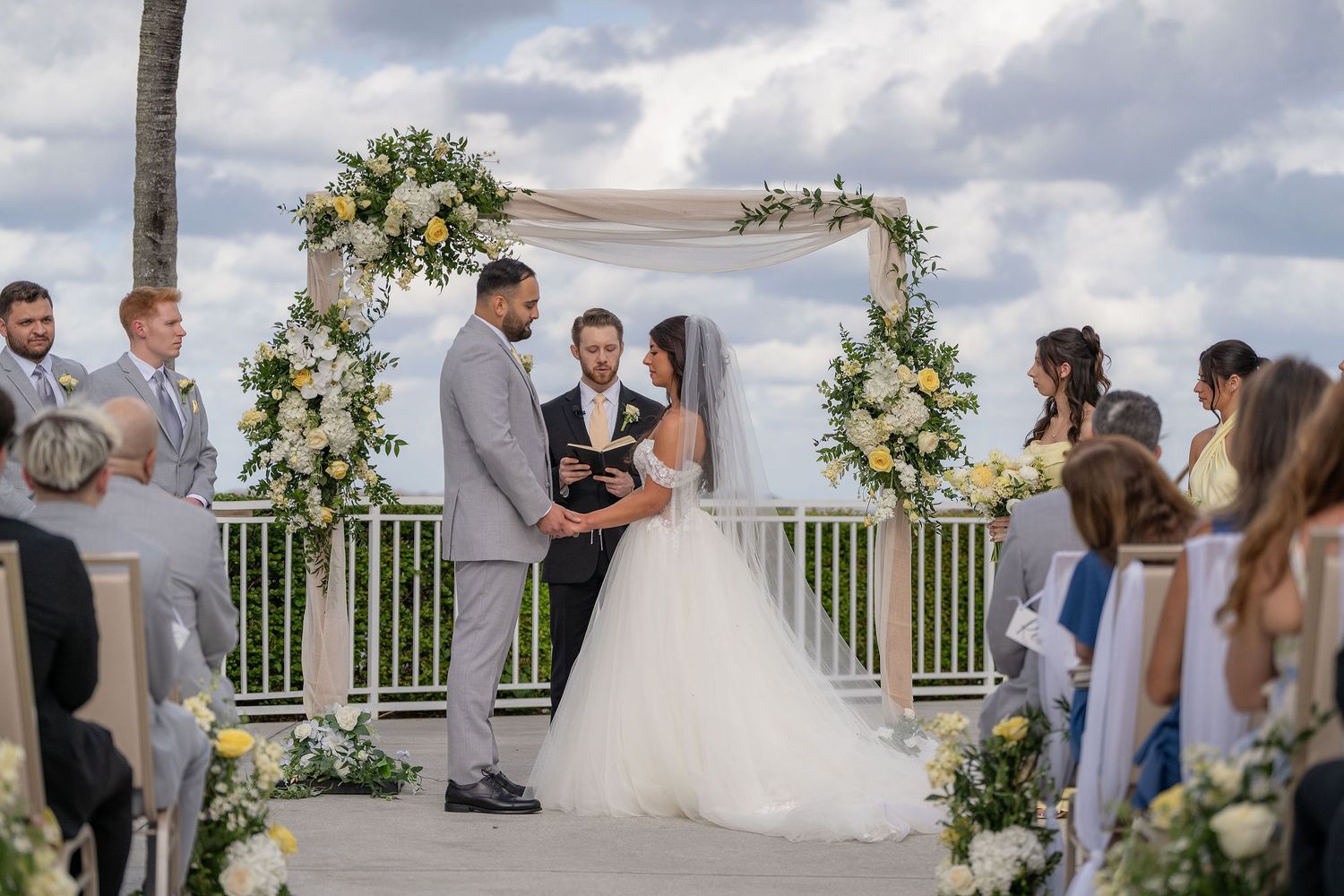 Couple exchanging vows beneath a floral arch on the North Terrace at the Mansion at Tuckahoe