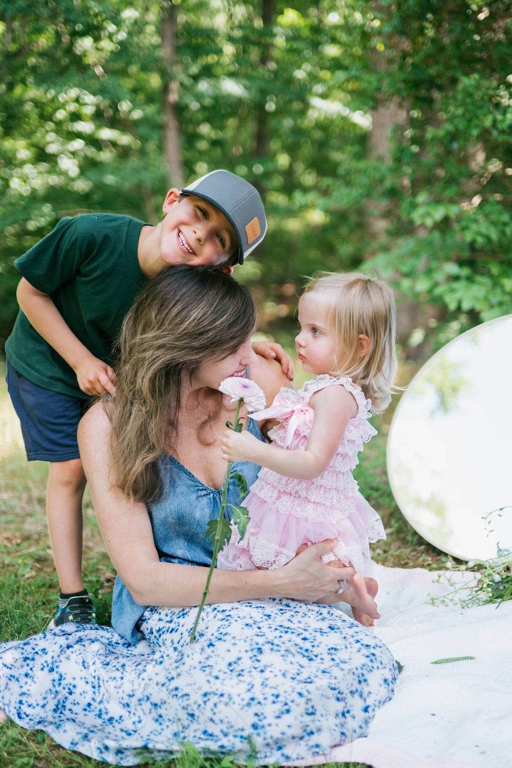 Mother in blue floral dress with young son and toddler daughter in pink dress playing outdoors in a garden in North Carolina