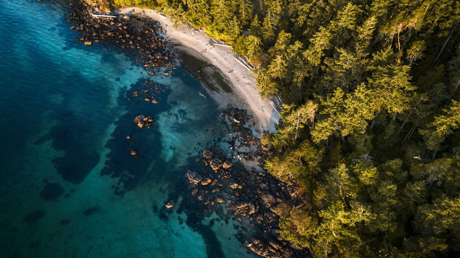 Aerial view of a secluded sandy beach with turquoise water, rocky shoreline, and lush green forest canopy.