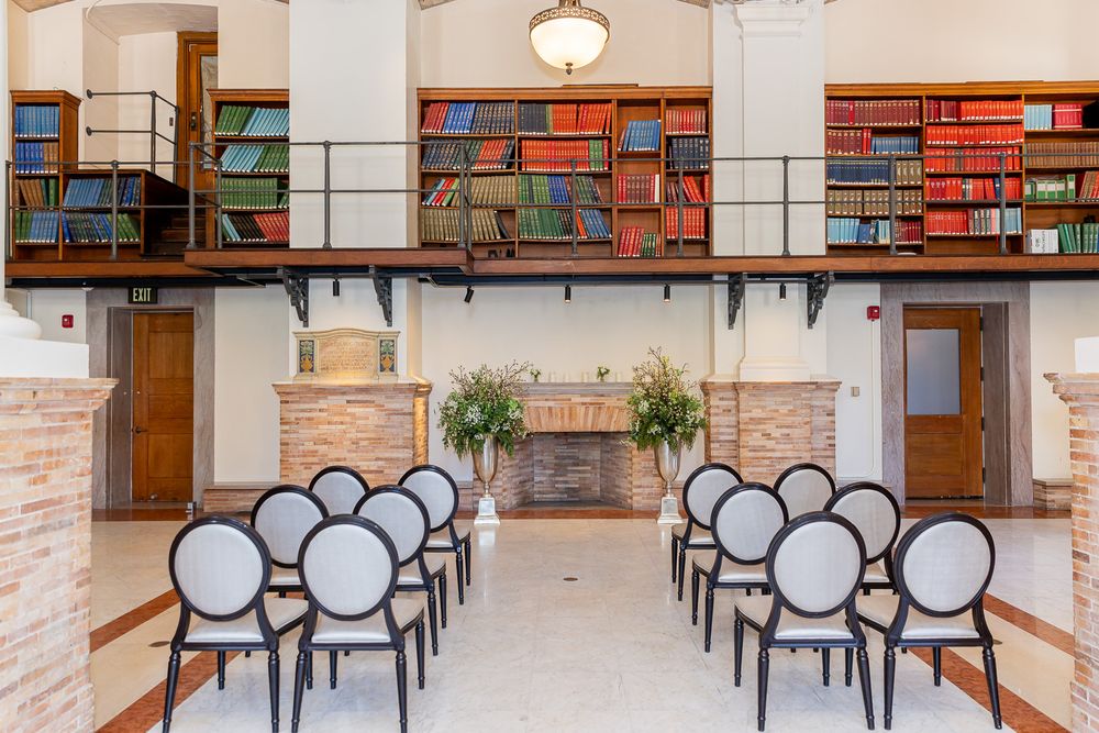 Elegant ceremony room with black chairs, fireplace, and mezzanine library with colorful books.