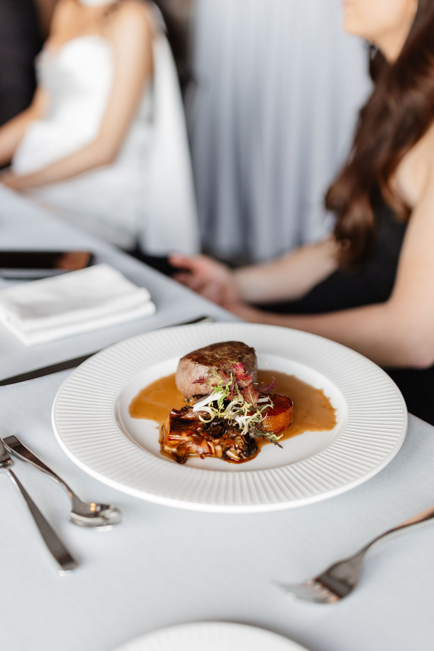 Elegant fine dining plate with seared meat, rich sauce, and garnish on white plate in upscale restaurant setting.
