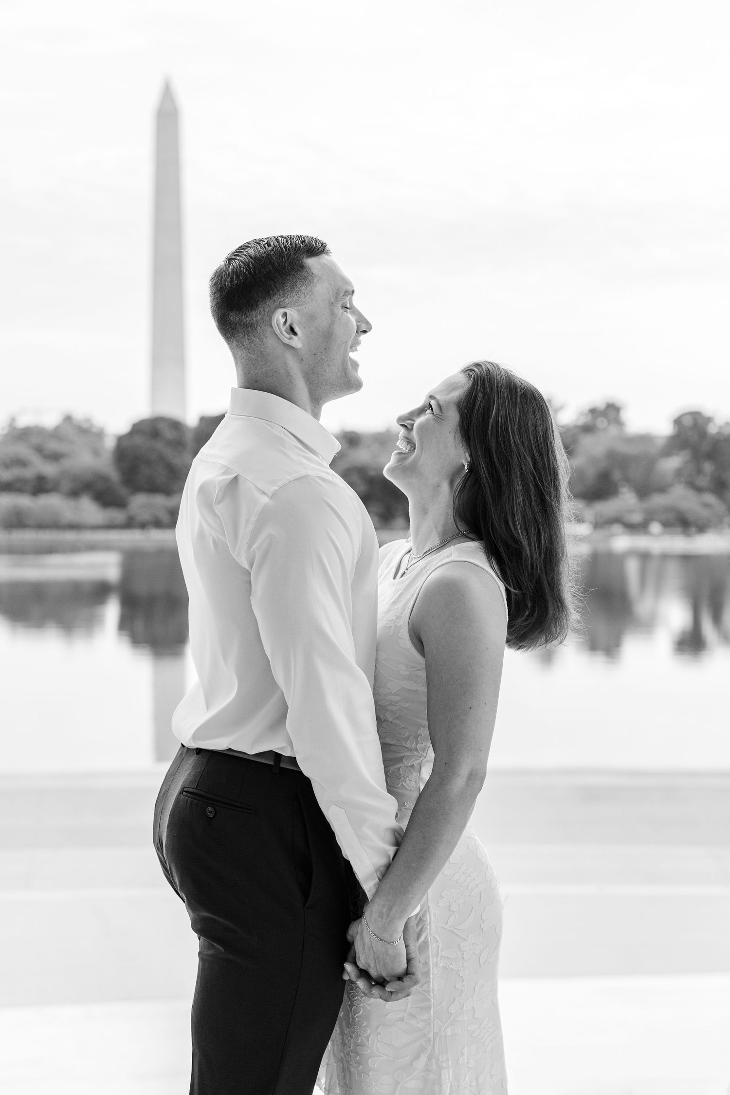 Black and white photo of a couple holding hands and laughing near the Washington Monument reflecting pool.