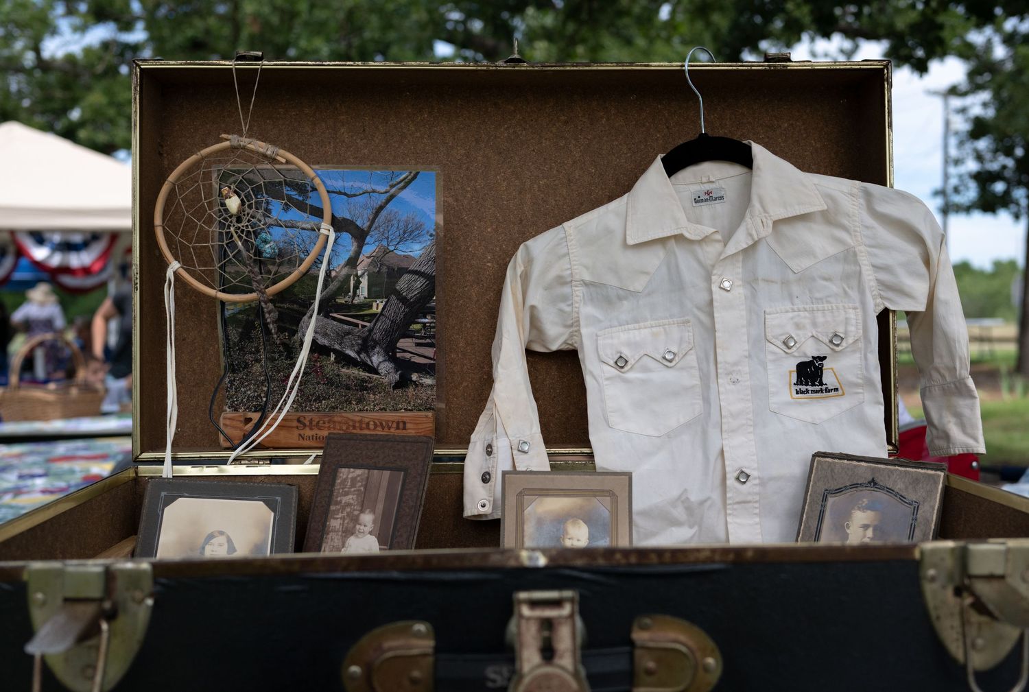 Vintage suitcase display with white denim jacket, dreamcatcher, framed photos, and artwork at an outdoor flea market.