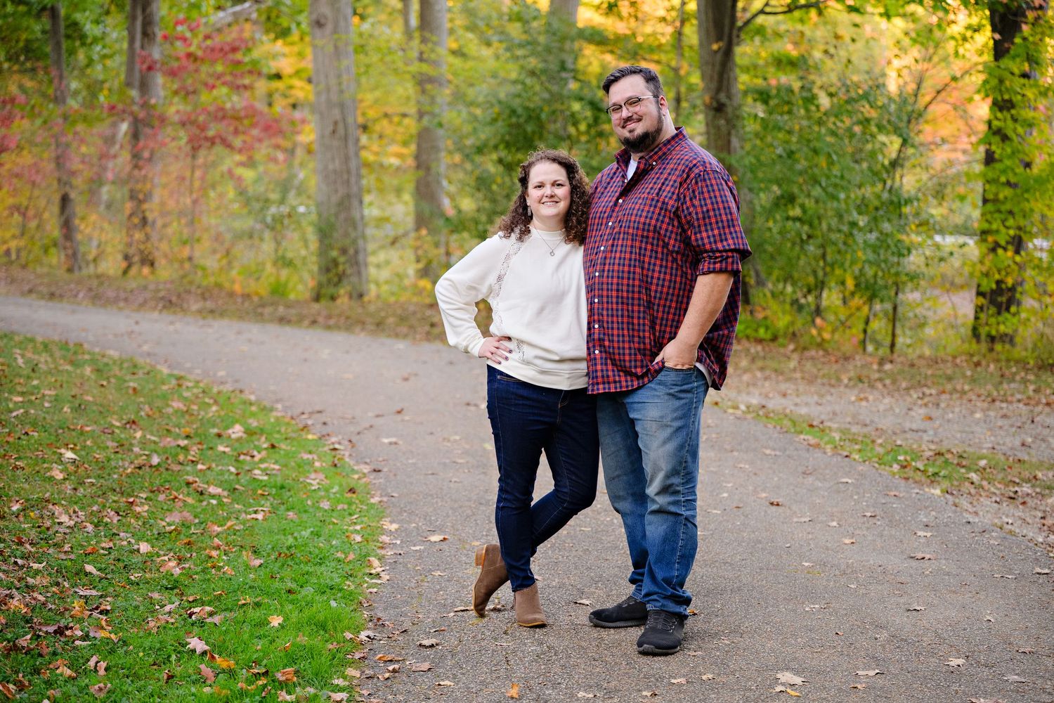 Newly engaged couple wearing casual clothing standing on a trail at Squires Castle in the fall with colorful foliage around them.
