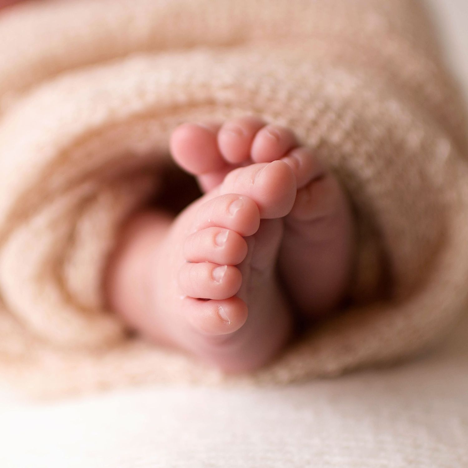 Sleeping newborn baby girl wrapped in pink knit blanket wearing white flower headband on white background.