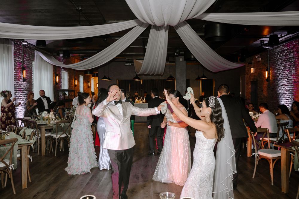 Bride and groom dancing with wedding guests in a decorated reception hall with elegant white draping.