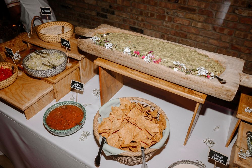 A buffet table with tortilla chips, salsa, guacamole on a wooden board, and assorted dips at a catered event.
