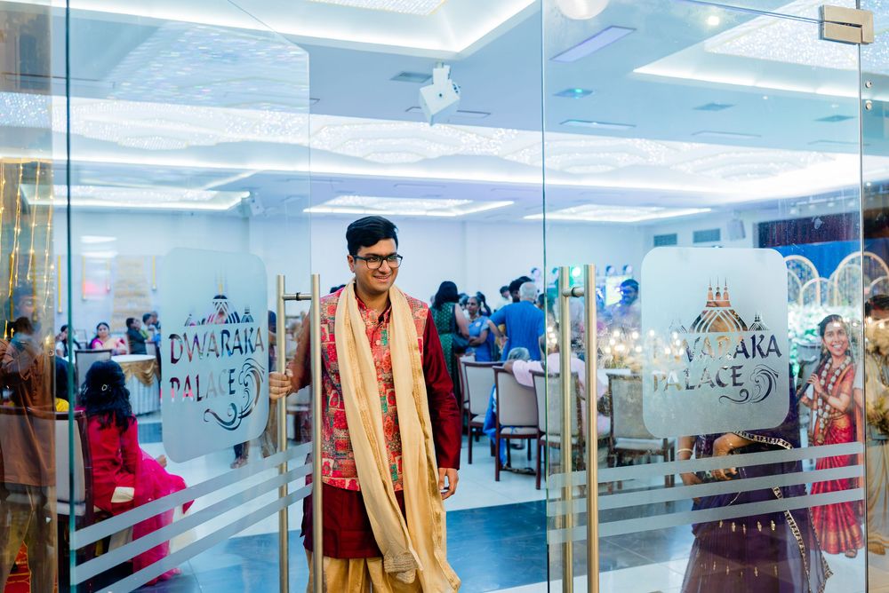 Man in traditional Indian attire smiling at a wedding venue entrance with decorated glass doors.