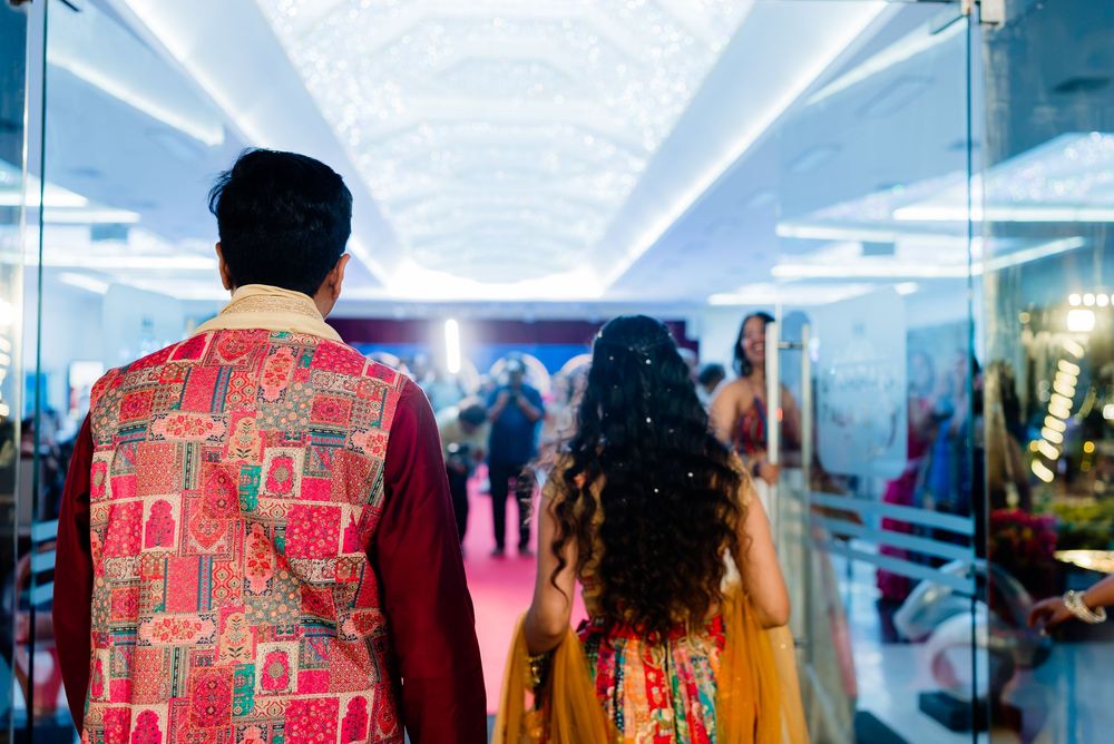 Couple in vibrant Indian wedding attire walking through an elegant decorated hallway during a traditional ceremony.
