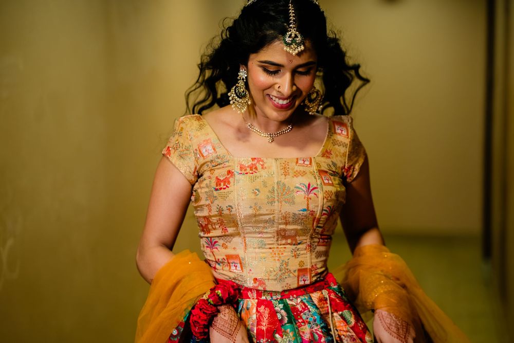 Smiling bride in colorful embroidered lehenga choli with gold maang tikka and traditional jewelry at Indian wedding.