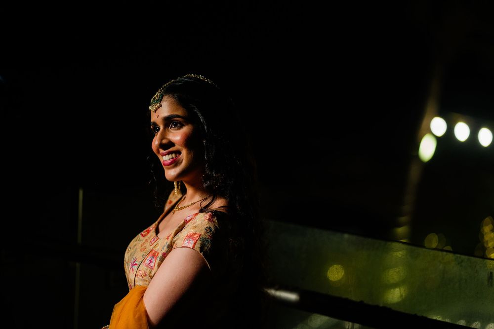 A smiling Indian bride in traditional attire glows under dramatic lighting at a nighttime celebration.