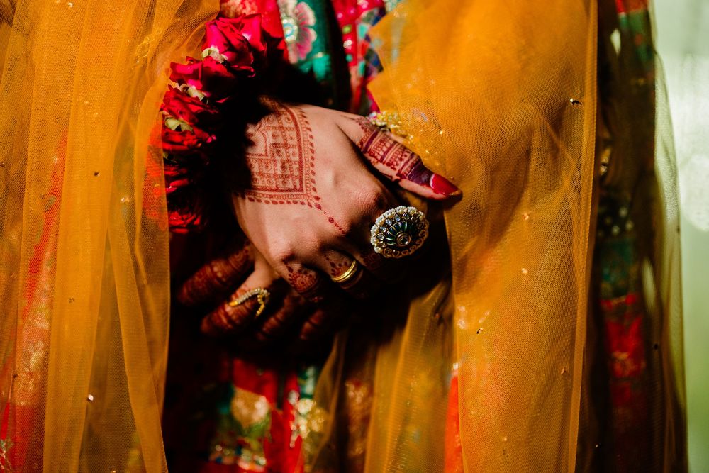 Close-up of Indian bride hands adorned with henna mehndi, gold rings, and a watch, draped in a yellow dupatta.