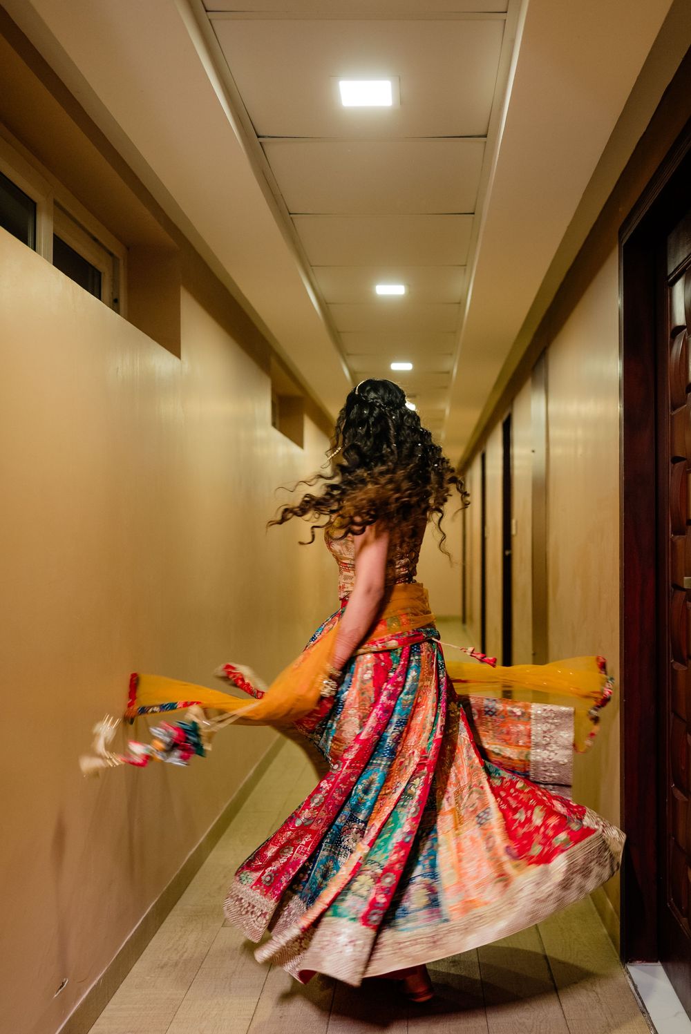Indian woman in colorful lehenga twirling in a hotel corridor during a wedding celebration.