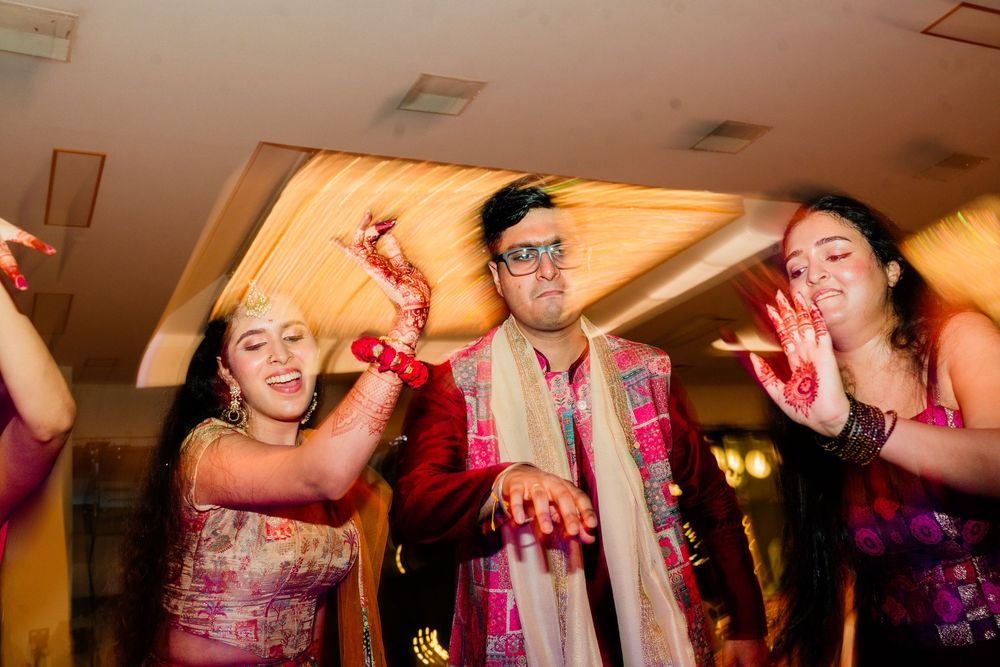 Three guests with henna-decorated hands dancing joyfully at an Indian wedding party.