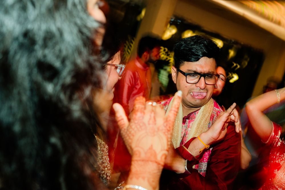 Man in glasses and red traditional attire clapping hands during Indian wedding ceremony.