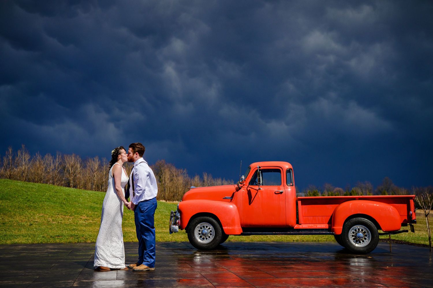 Bride and Groom kissing near the bright red truck beneath a stormy sky after their wedding at 1885 Farms in Navarre Ohio during the Spring.