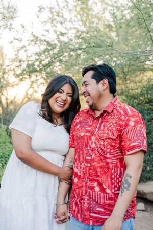 Happy Latino couple laughing together outdoors in golden hour light, man in red Hawaiian shirt.