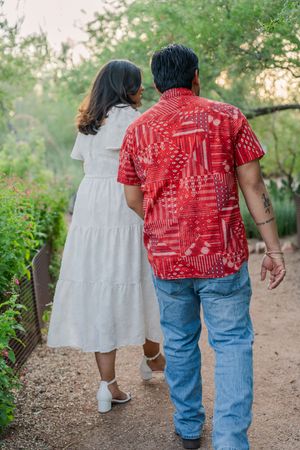 Couple walking hand-in-hand down a garden path, woman in white dress and man in red shirt.