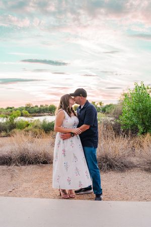 Couple sharing a romantic kiss at sunset in a desert landscape with colorful pink and blue sky.