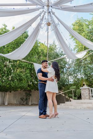 Couple embraces and dances under elegant white draped canopy with chandelier in outdoor venue.