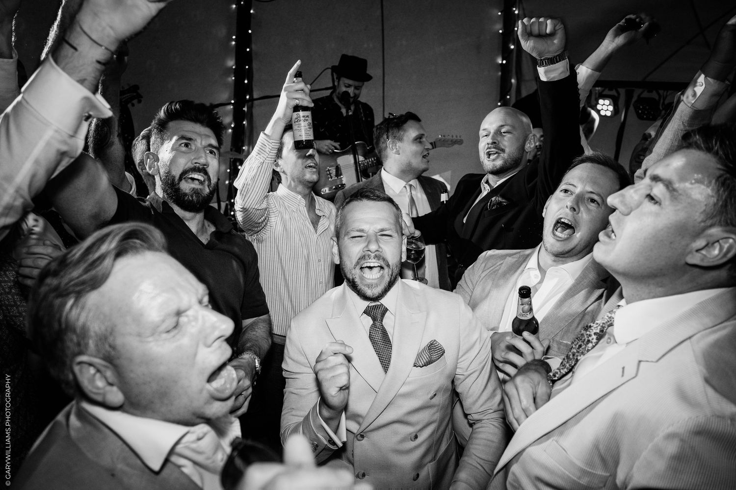Black and white photo of joyful men celebrating at a wedding reception party, laughing and raising drinks.