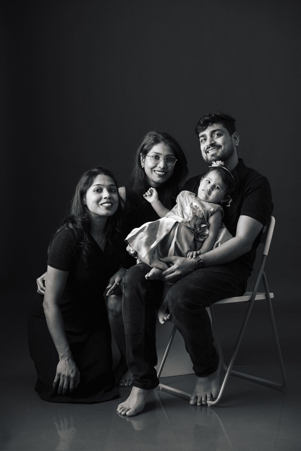 Black and white family portrait with two women, a man, and a baby posing together in a studio setting.