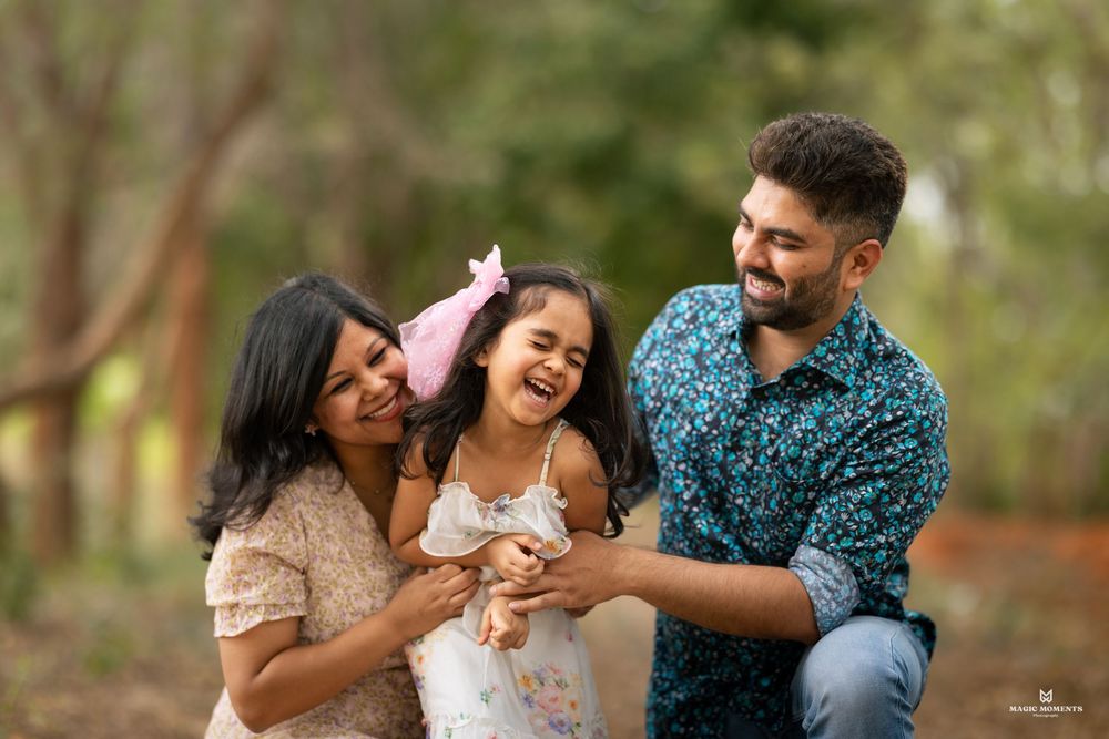 Happy Indian family with parents and young daughter laughing together outdoors in a lush green park setting.