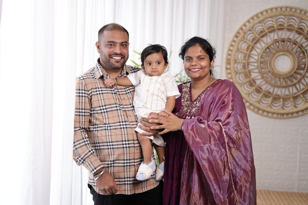 South Asian family portrait with parents and baby dressed in traditional and casual attire at a celebration.