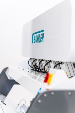 Bühler industrial food processing machine with teal logo, featuring cables and control panel components.