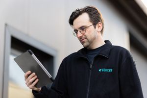 A man examines a tablet computer outdoors near an industrial building.