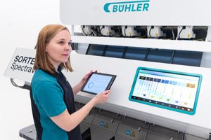 Woman operating a Bühler SORTEX Spectra sorting machine using a tablet and touchscreen control panel.