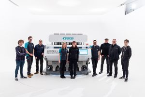 Team of professionals posing with a Buhler Sortex optical sorting machine in a bright white studio setting.