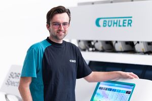 Bühler technician smiling beside a Bühler machine control panel in a modern industrial facility.