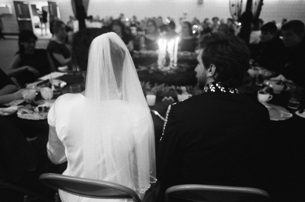 Black and white photo of bride and groom seated at wedding reception table with candles glowing behind them.