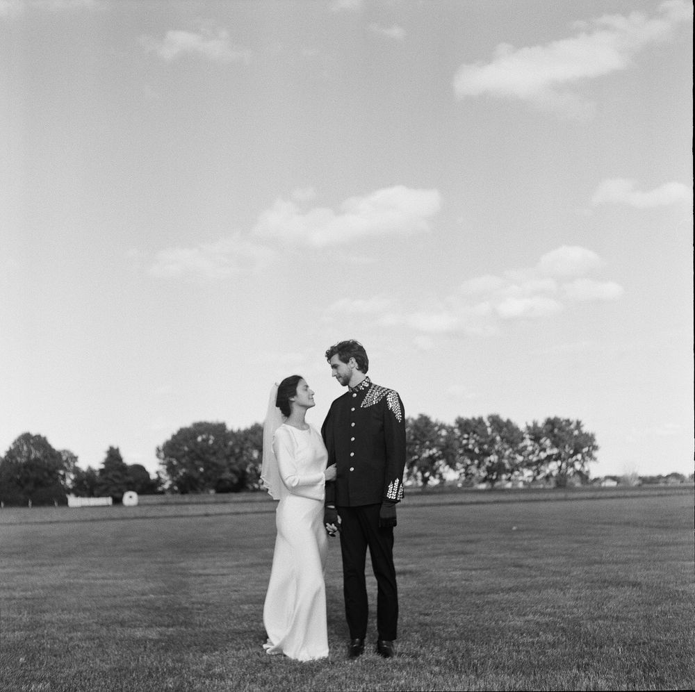 Black and white photo of a bride and groom in military uniform standing in a field on their wedding day.