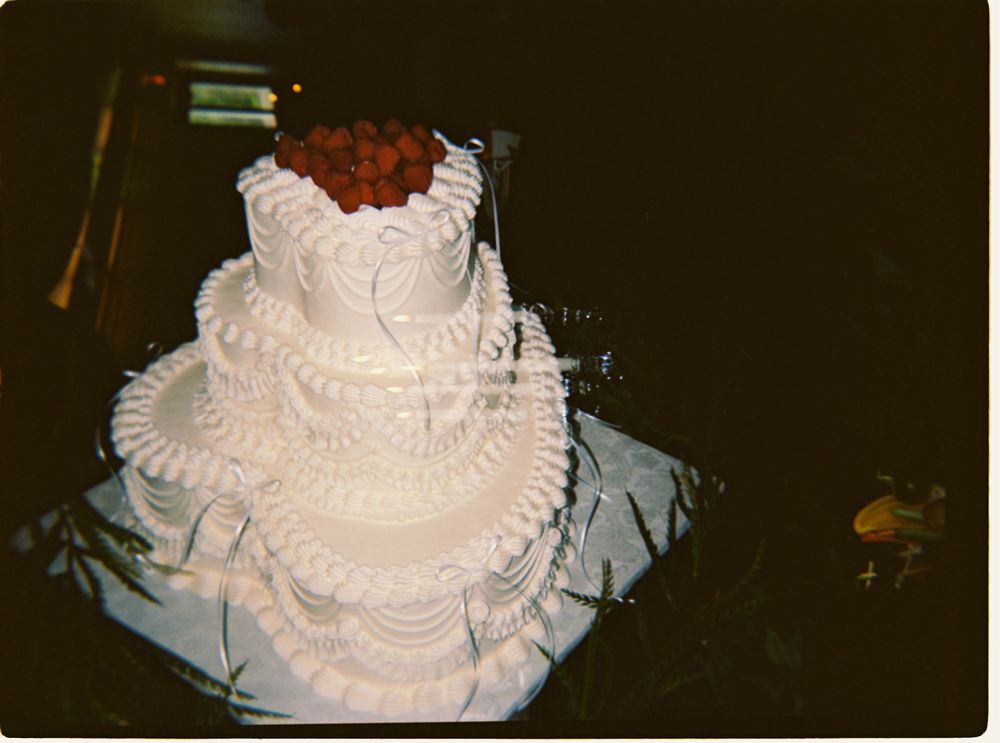 Elegant three-tier white wedding cake decorated with intricate frosting and topped with red roses.