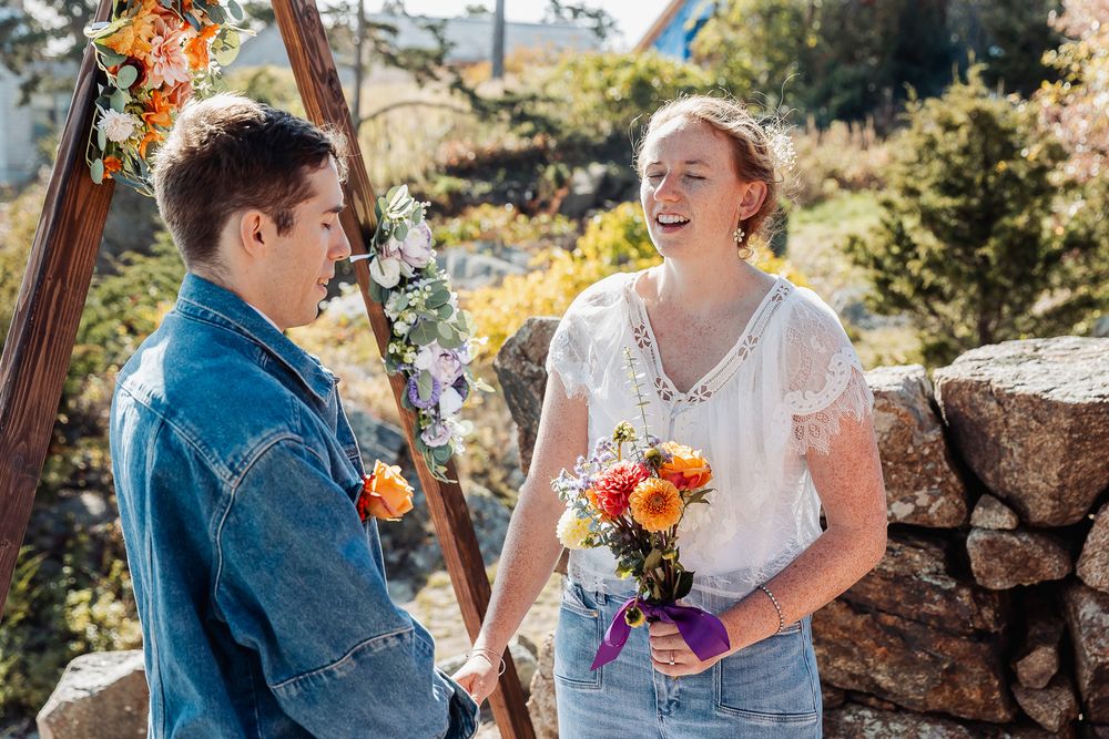 Couple holding hands and laughing during outdoor wedding ceremony with floral arch and stone wall backdrop.