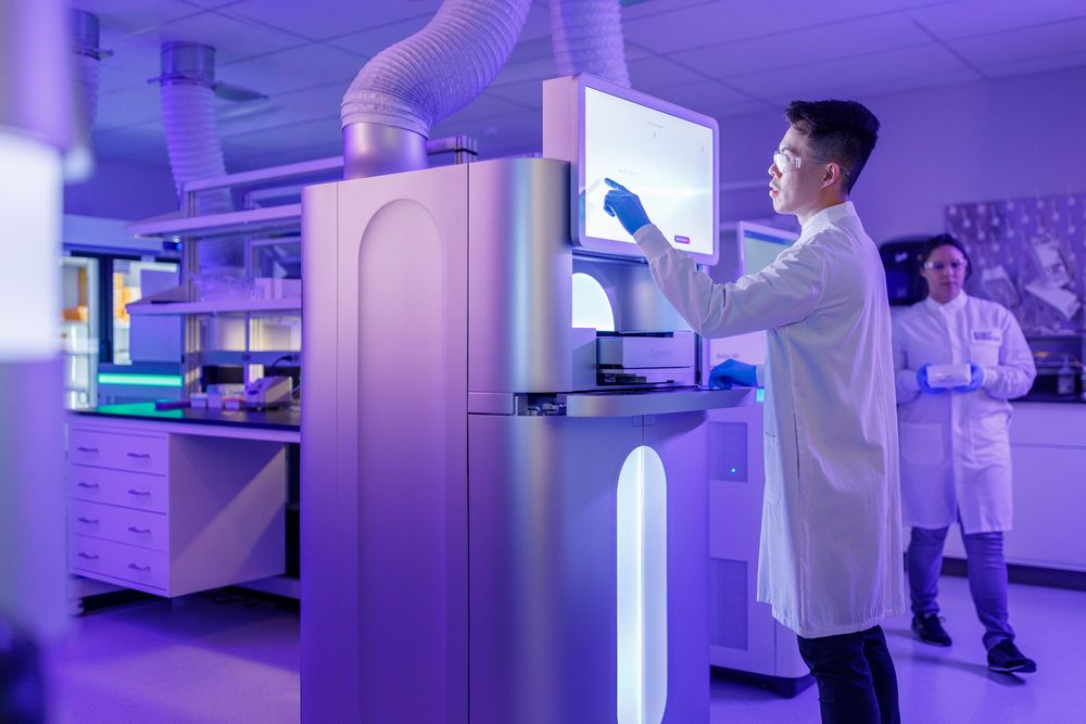 Scientists in white lab coats operating advanced genomic sequencing equipment in a modern blue-lit research laboratory.