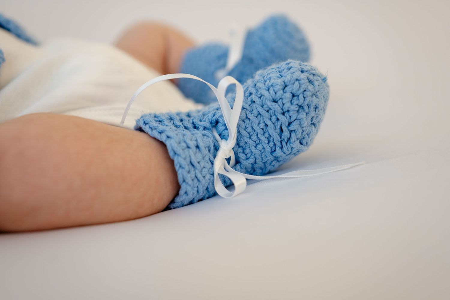 Close-up of a baby's feet wearing blue knitted booties with white ribbon ties on a white background.
