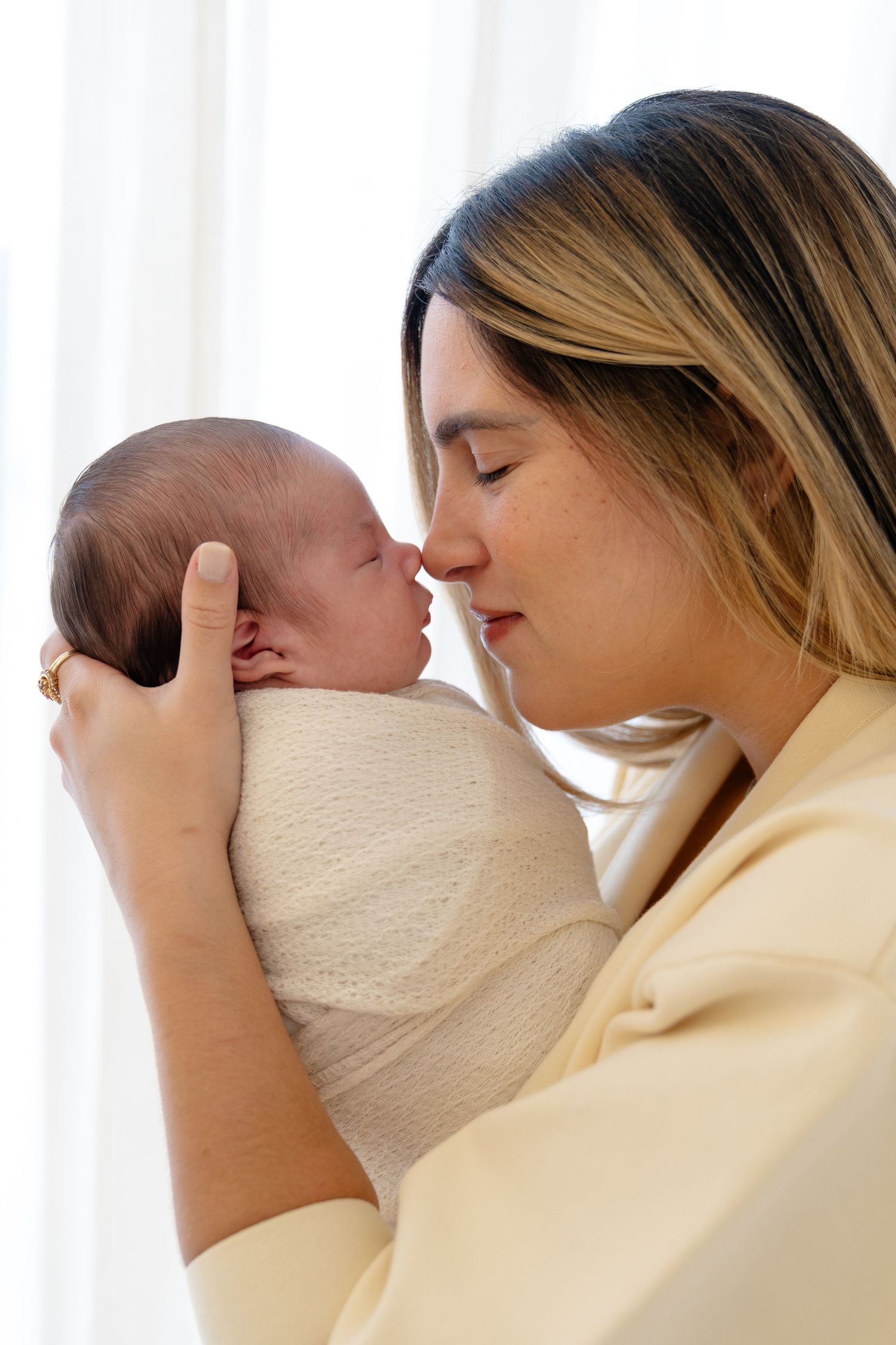 A tender moment as a young mother with blonde highlights gently nuzzles her swaddled newborn baby.