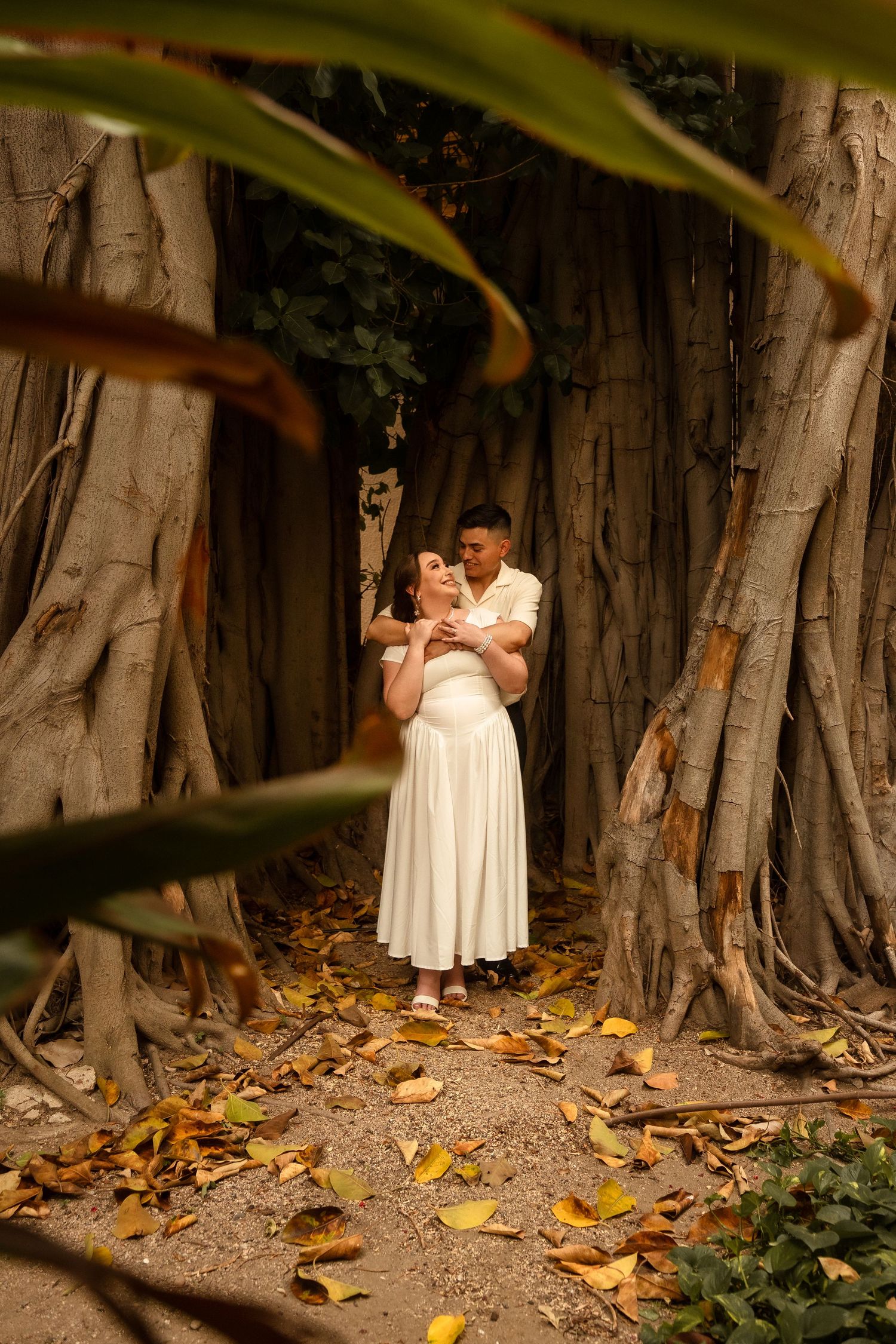 Couple sharing a romantic embrace on a wooden bridge, framed by iron railings and a red-tiled roof building.