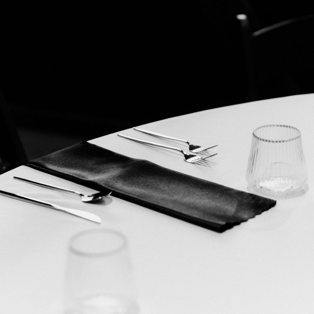 Elegant black and white fine dining table setting with silverware, folded napkin, and crystal glassware on white tablecloth.