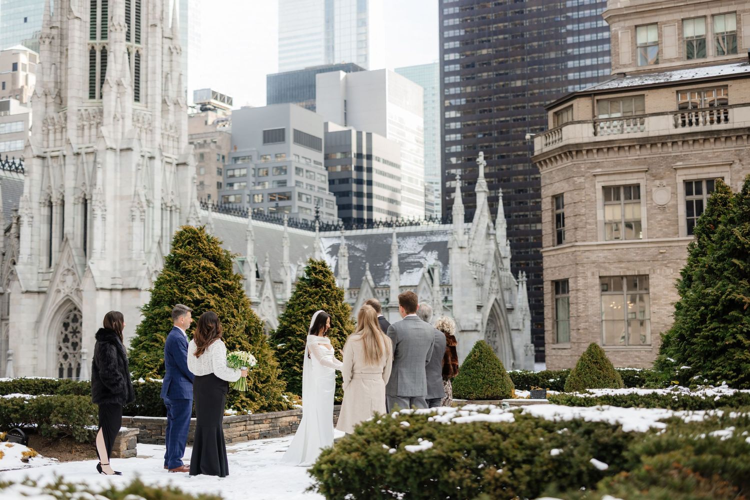 Small winter rooftop wedding ceremony with snow, gothic cathedral spires, and city skyscrapers in New York City.