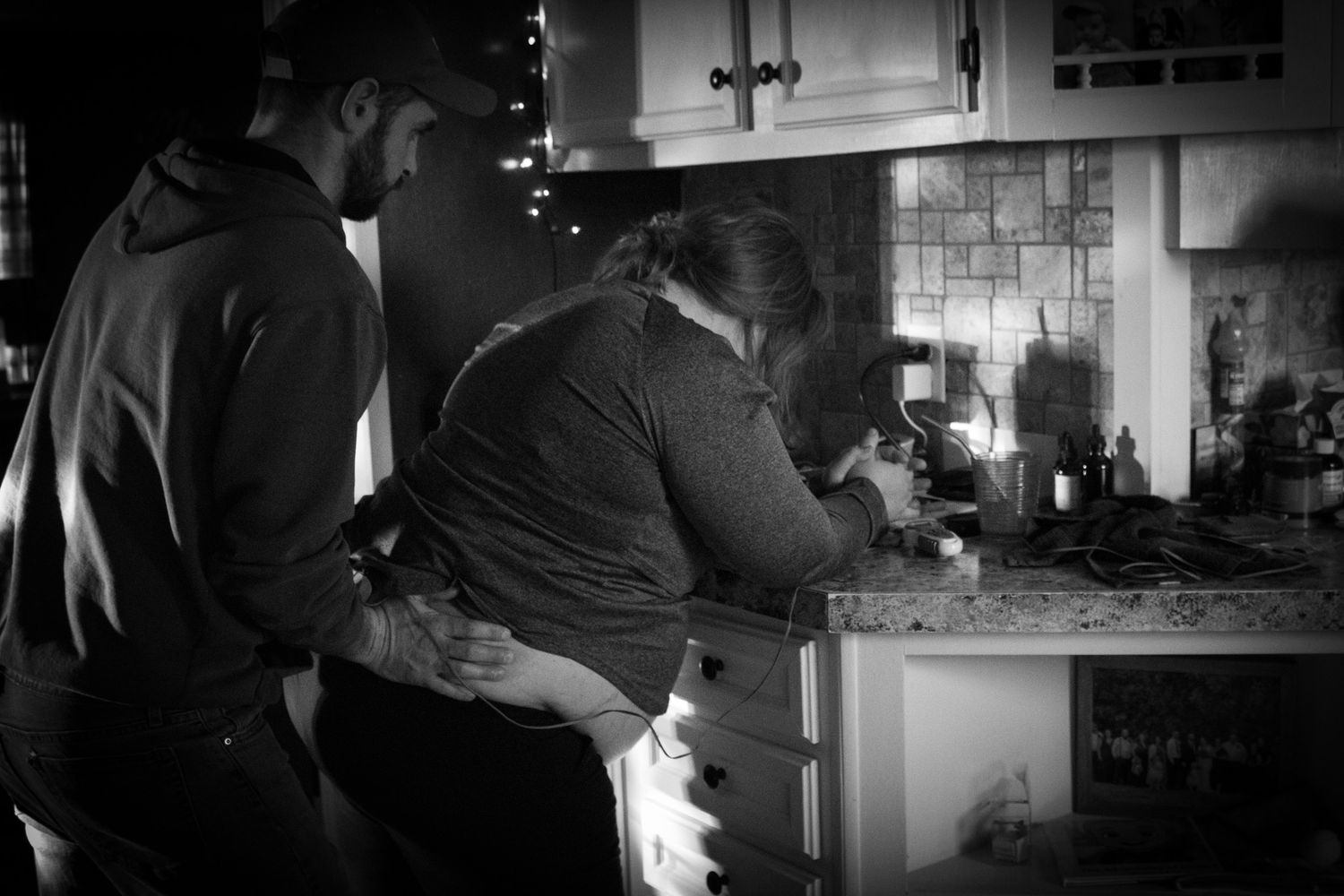 Couple sharing an intimate moment together in a dimly lit kitchen during labor.