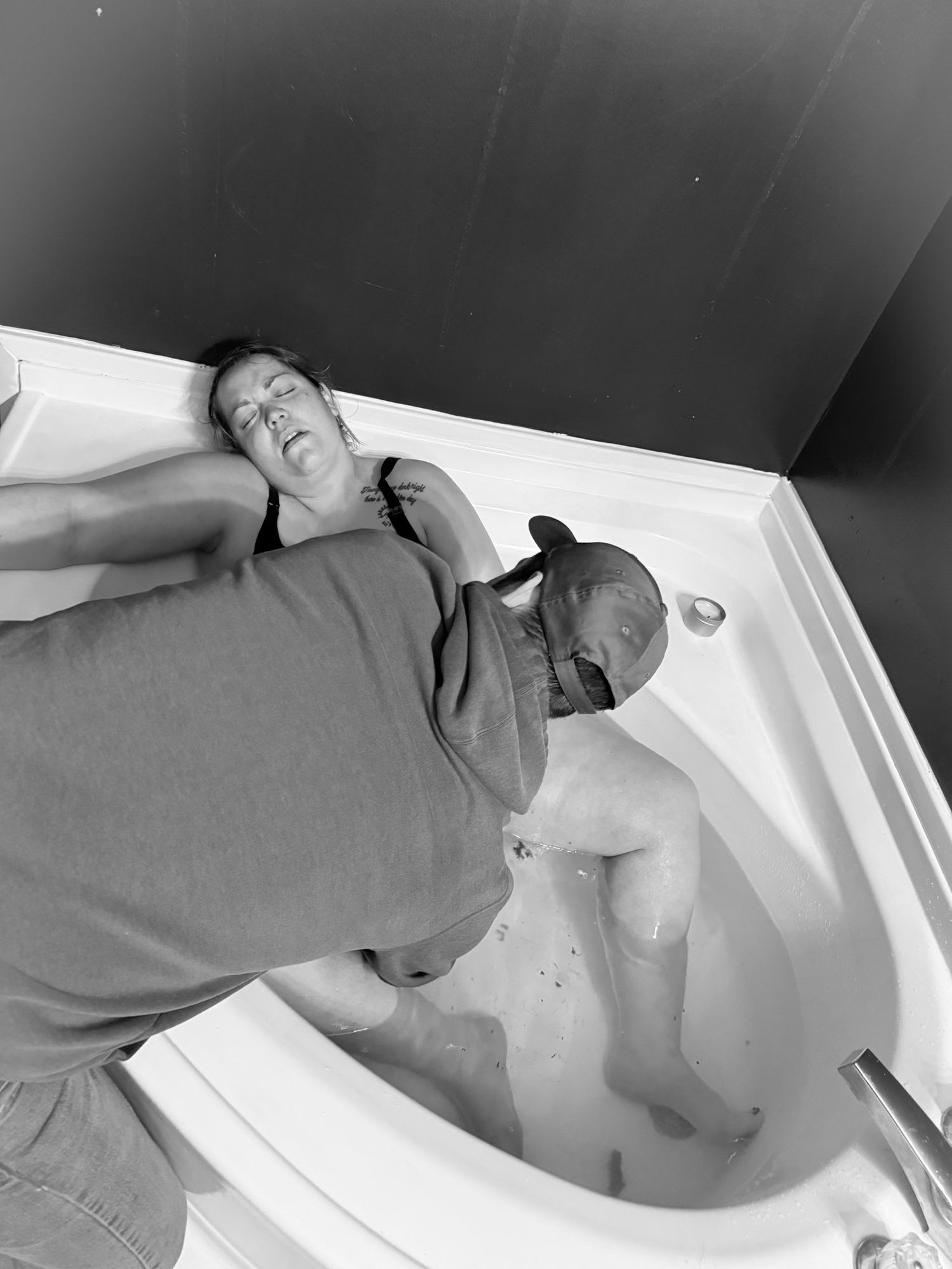 Black and white photo of a woman in labor in a bathtub with supportive partner nearby.
