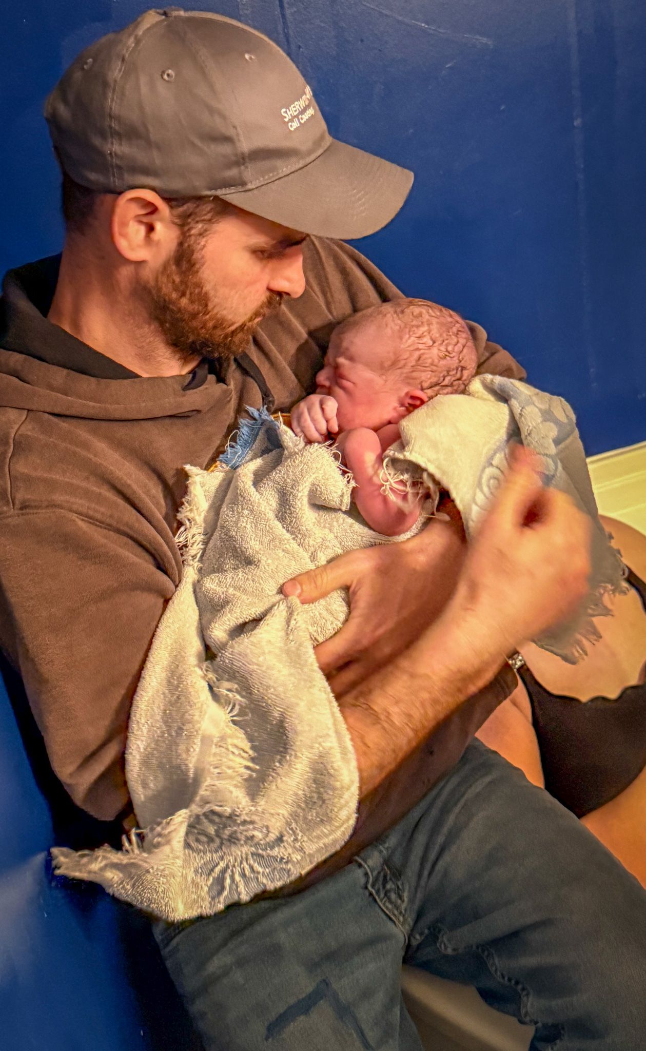 New father in a gray cap tenderly holding his newborn baby in a blanket.