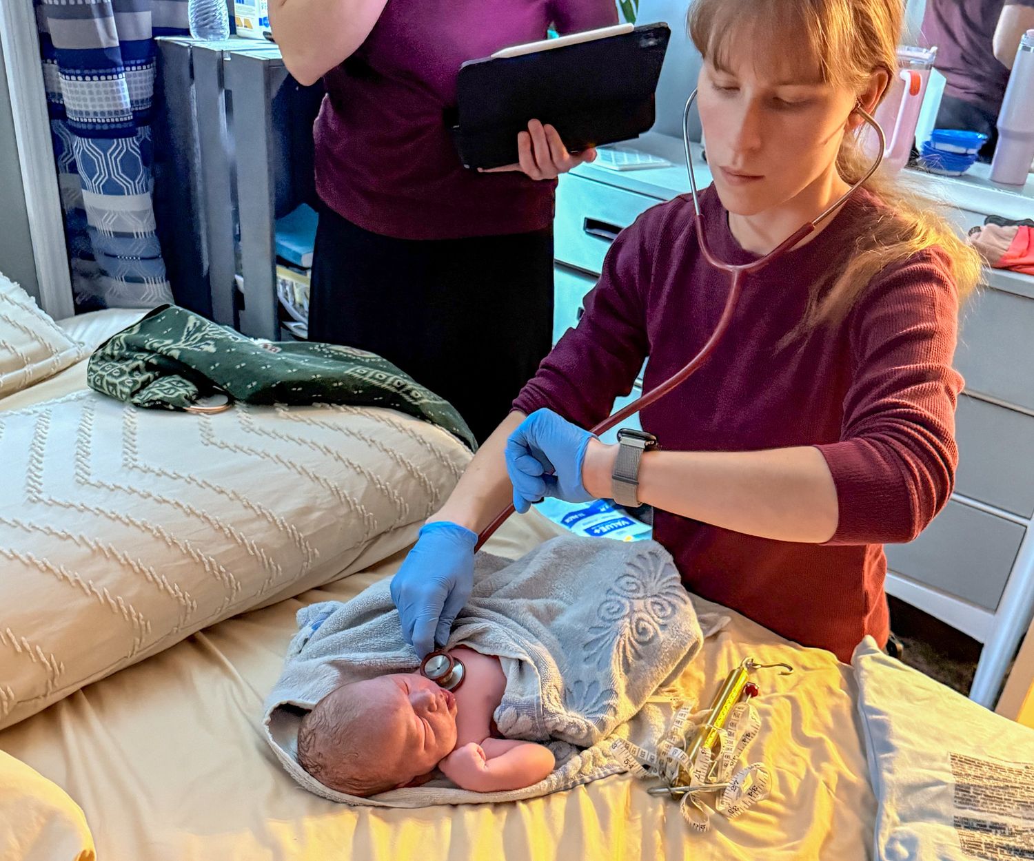 Midwife carefully examining a newborn baby on a bed after home birth.